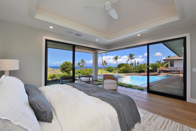 bedroom featuring light hardwood / wood-style flooring, a tray ceiling, and multiple windows