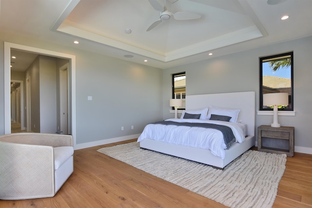 bedroom with a tray ceiling, light wood-type flooring, and ceiling fan