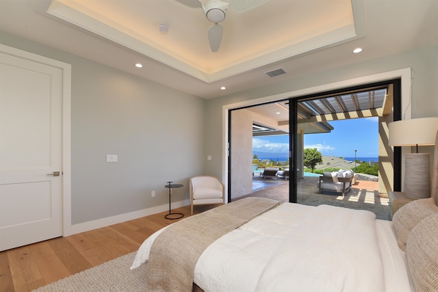 bedroom with a raised ceiling, access to exterior, light wood-type flooring, and ceiling fan