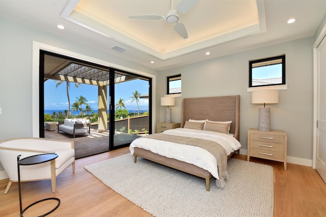 bedroom featuring light hardwood / wood-style floors, access to exterior, a tray ceiling, and ceiling fan