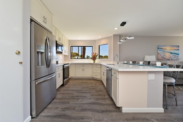 kitchen with sink, dark wood-type flooring, stainless steel appliances, kitchen peninsula, and pendant lighting