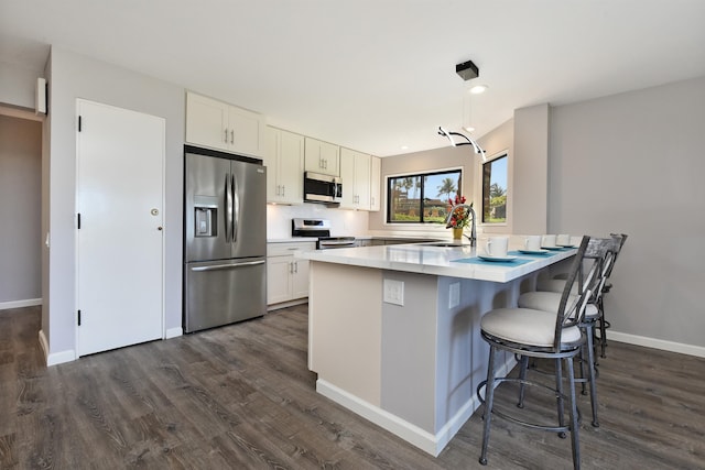 kitchen featuring appliances with stainless steel finishes, a center island, white cabinetry, dark hardwood / wood-style flooring, and a kitchen breakfast bar