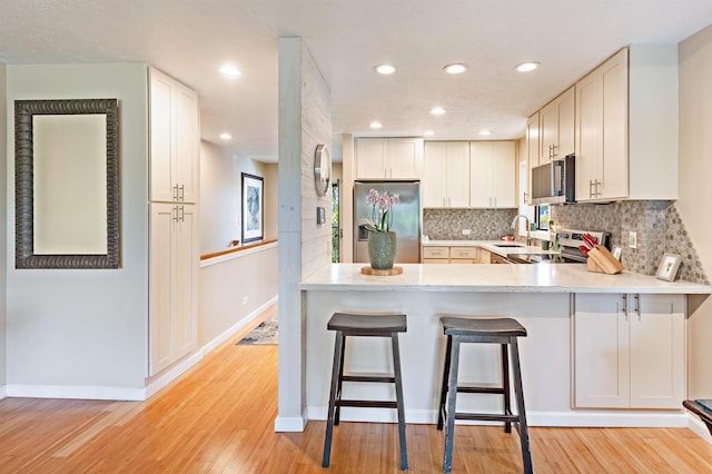 3788 Lower Honoapiilani Rd Unit D101, Lahaina, HI 96761 - kitchen with appliances with stainless steel finishes, light wood-type flooring, tasteful backsplash, a breakfast bar area, and a peninsula