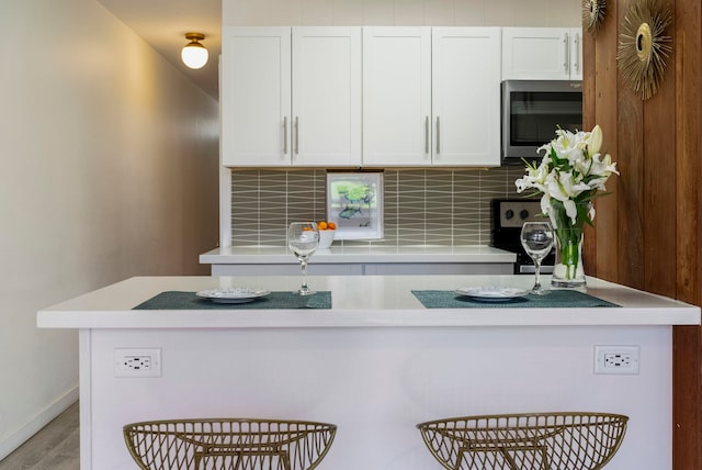 kitchen with backsplash, white cabinetry, light hardwood / wood-style flooring, and stove