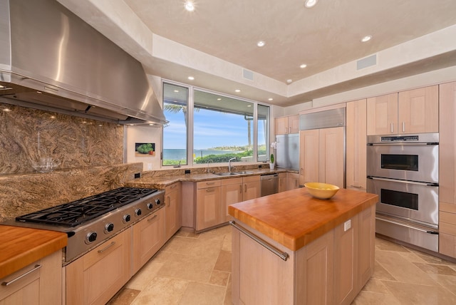 kitchen with butcher block countertops, wall chimney exhaust hood, stainless steel appliances, and a kitchen island