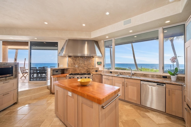 kitchen featuring appliances with stainless steel finishes, wall chimney exhaust hood, sink, a water view, and a center island