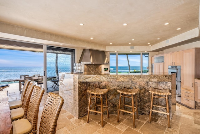 kitchen featuring a water view, wall chimney exhaust hood, a healthy amount of sunlight, and a breakfast bar area