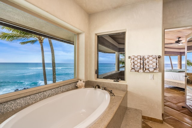 bathroom with tiled bath, a water view, plenty of natural light, and ceiling fan