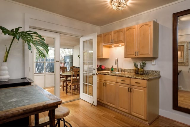 kitchen with light brown cabinetry, sink, ornamental molding, and light wood-type flooring