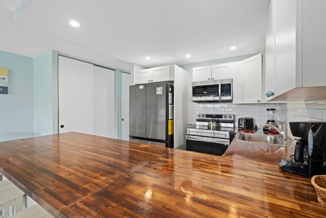 kitchen with backsplash, stainless steel appliances, butcher block counters, white cabinetry, and sink