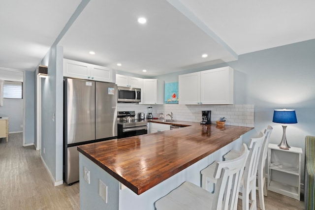 kitchen featuring light hardwood / wood-style flooring, backsplash, white cabinetry, appliances with stainless steel finishes, and kitchen peninsula