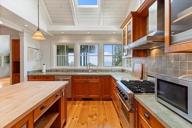 kitchen featuring light wood-type flooring, appliances with stainless steel finishes, decorative light fixtures, sink, and wall chimney exhaust hood