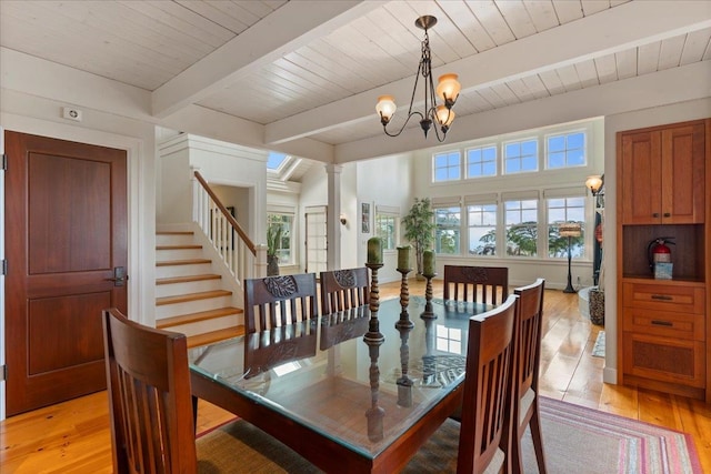 dining space featuring light wood-type flooring, an inviting chandelier, a healthy amount of sunlight, and beam ceiling