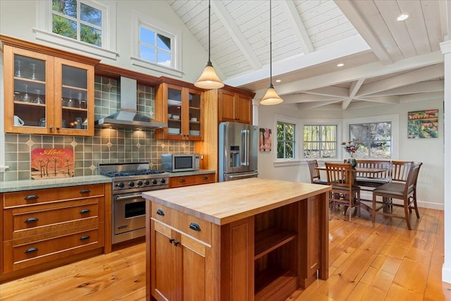 kitchen with appliances with stainless steel finishes, tasteful backsplash, wall chimney exhaust hood, light wood-type flooring, and butcher block countertops