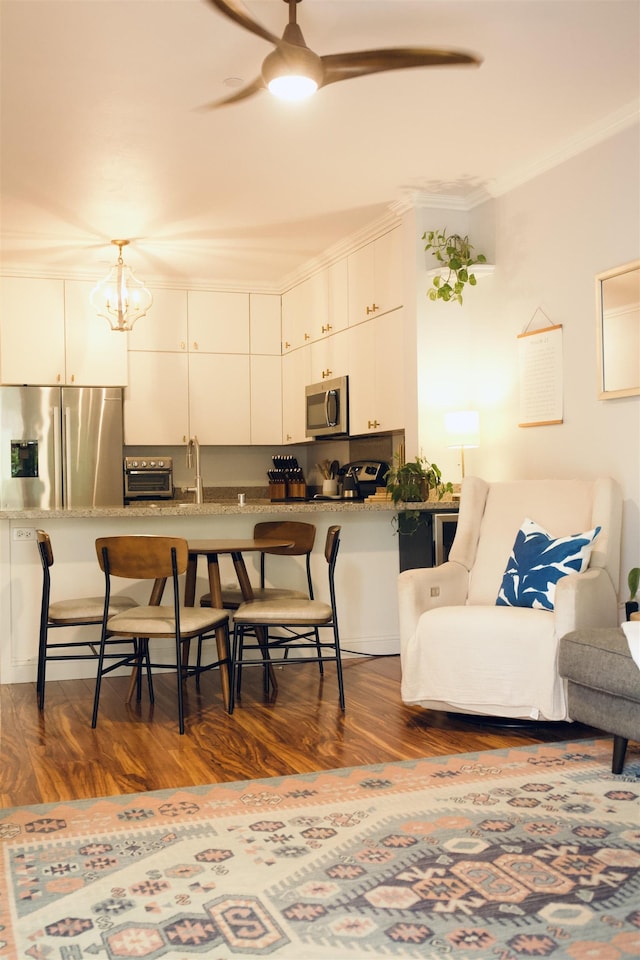 kitchen featuring appliances with stainless steel finishes, a breakfast bar, dark wood-style flooring, crown molding, and ceiling fan with notable chandelier