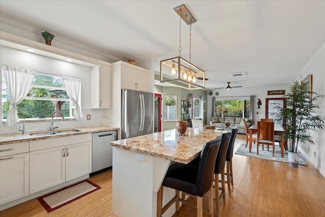 kitchen featuring a kitchen island, open floor plan, a sink, light wood-style flooring, and appliances with stainless steel finishes