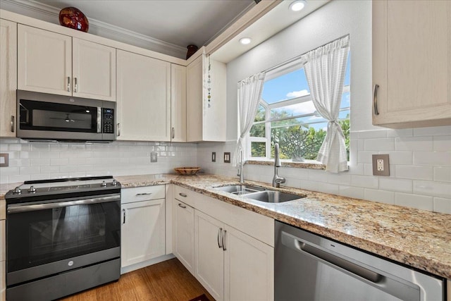kitchen with crown molding, light stone countertops, appliances with stainless steel finishes, a sink, and tasteful backsplash