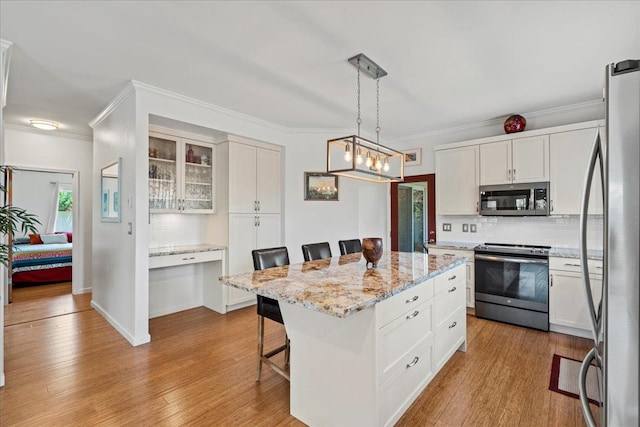 kitchen with decorative backsplash, a kitchen island, a kitchen bar, white cabinetry, and stainless steel appliances