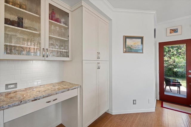 interior space with baseboards, tasteful backsplash, ornamental molding, and light wood finished floors