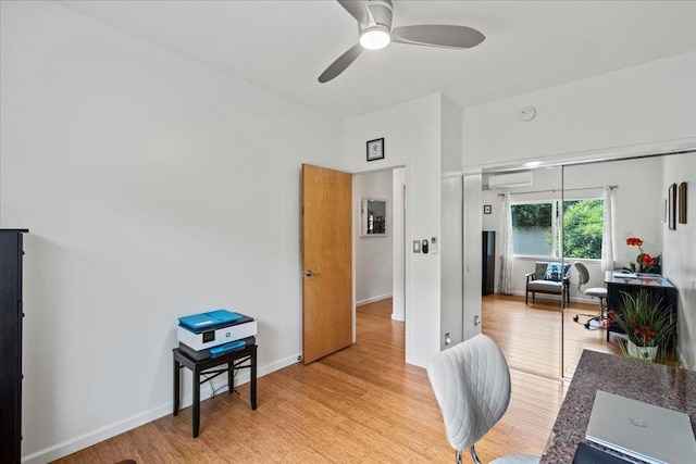 office area with baseboards, a ceiling fan, light wood-type flooring, and a wall mounted air conditioner