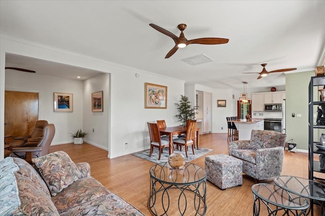 living area featuring crown molding, light wood-style flooring, a ceiling fan, baseboards, and visible vents