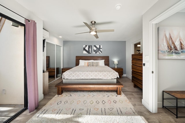 bedroom featuring light wood-type flooring, an AC wall unit, ceiling fan, and a closet