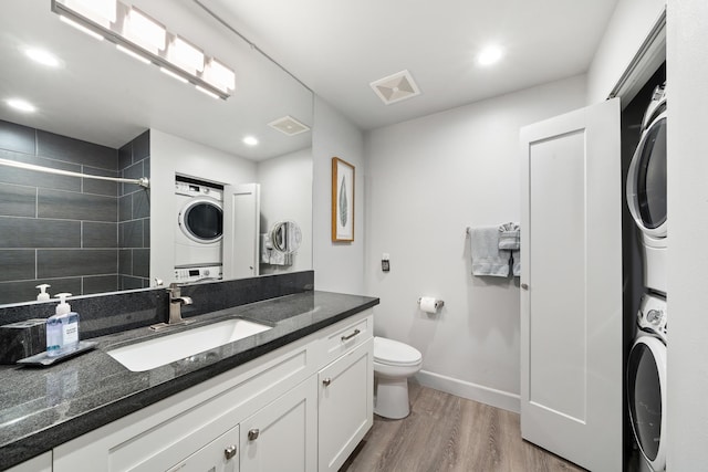 bathroom featuring stacked washing maching and dryer, toilet, vanity, a tile shower, and hardwood / wood-style flooring