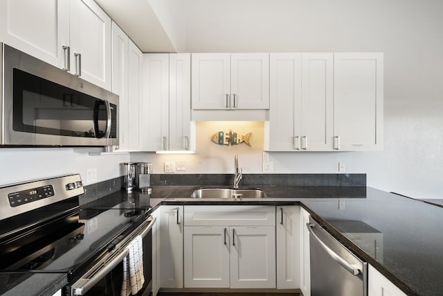 kitchen with appliances with stainless steel finishes, white cabinets, dark stone countertops, and sink