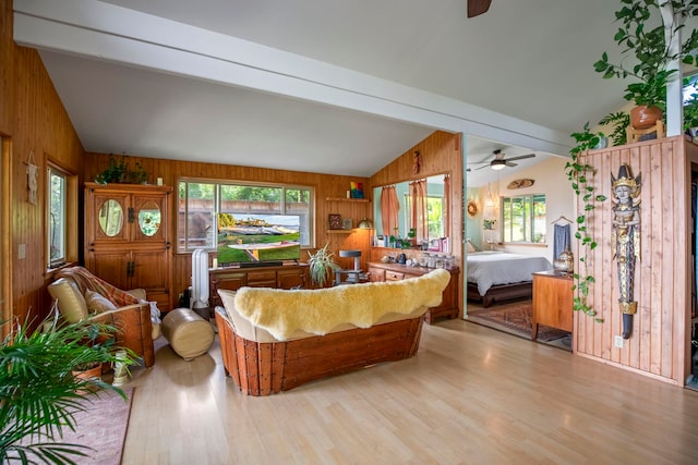 living room with plenty of natural light, light wood-type flooring, lofted ceiling with beams, and wooden walls