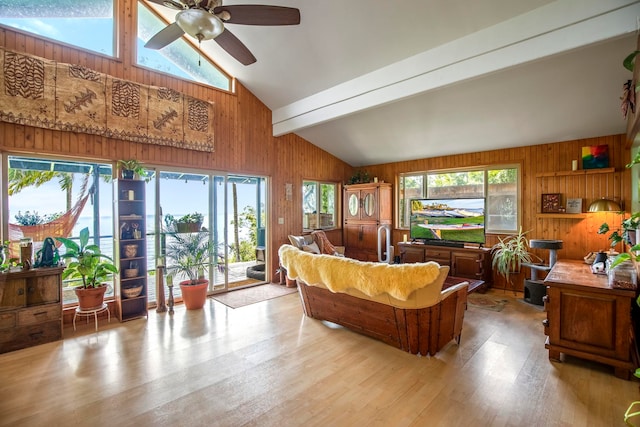 living room featuring ceiling fan, wood walls, light hardwood / wood-style flooring, and lofted ceiling with beams