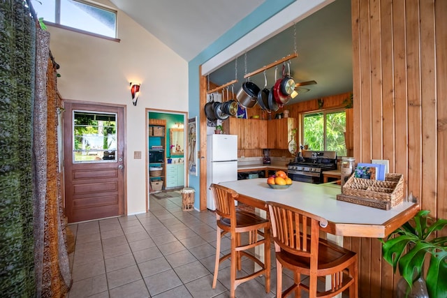 kitchen featuring white refrigerator, wooden walls, kitchen peninsula, vaulted ceiling, and a breakfast bar area