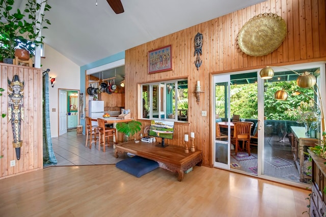 interior space featuring wood walls, light hardwood / wood-style flooring, high vaulted ceiling, and ceiling fan