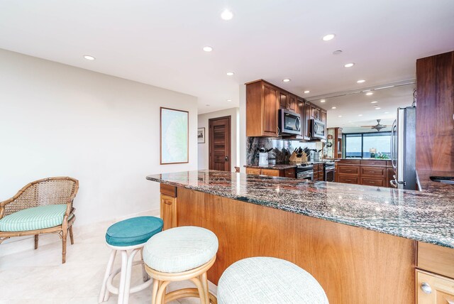 kitchen featuring kitchen peninsula, decorative backsplash, dark stone counters, and appliances with stainless steel finishes