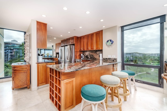 kitchen featuring expansive windows, backsplash, kitchen peninsula, stainless steel fridge, and dark stone counters