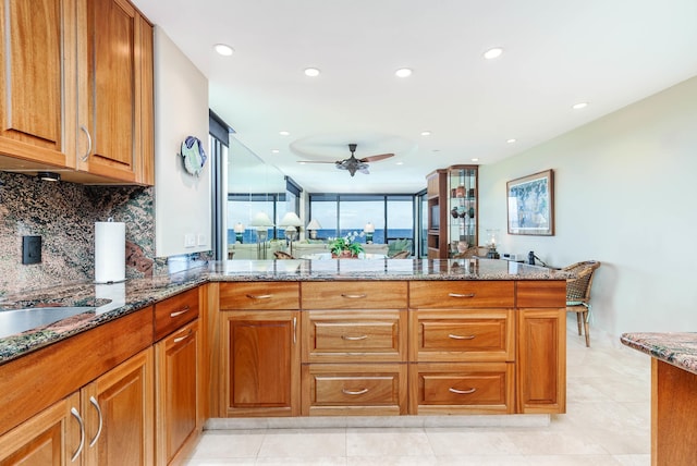 kitchen with ceiling fan, decorative backsplash, dark stone countertops, light tile patterned flooring, and kitchen peninsula