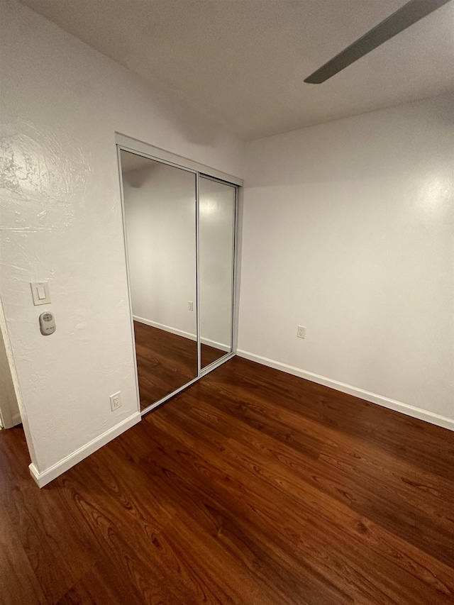 unfurnished bedroom with ceiling fan, a closet, and dark wood-type flooring