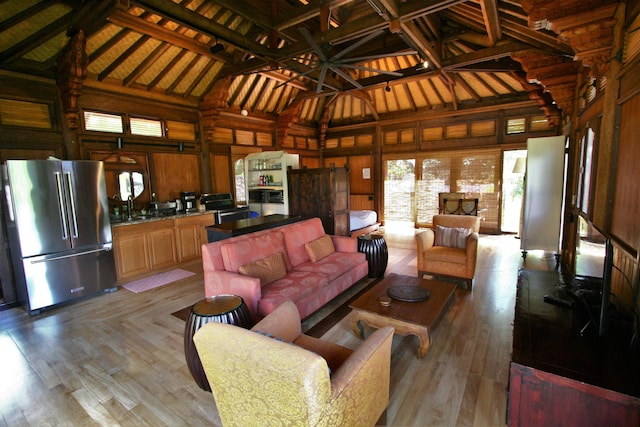 living room featuring beamed ceiling, light wood-type flooring, wooden walls, and sink