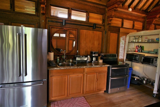 kitchen featuring wooden walls, stainless steel appliances, sink, dark stone counters, and light hardwood / wood-style floors