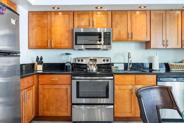 kitchen with appliances with stainless steel finishes, dark stone counters, and sink