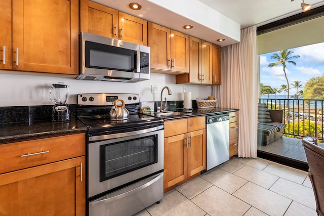 kitchen featuring sink, light tile patterned floors, dark stone counters, and appliances with stainless steel finishes