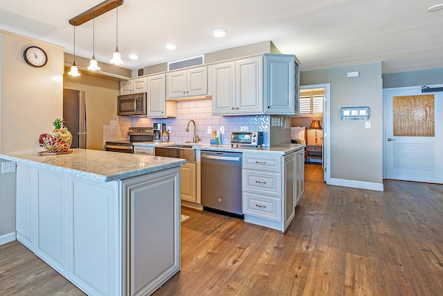 kitchen featuring kitchen peninsula, appliances with stainless steel finishes, decorative light fixtures, and hardwood / wood-style floors