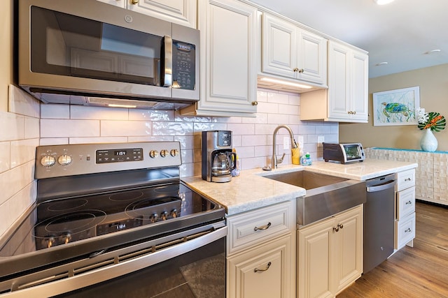 kitchen with backsplash, sink, light hardwood / wood-style flooring, white cabinetry, and stainless steel appliances