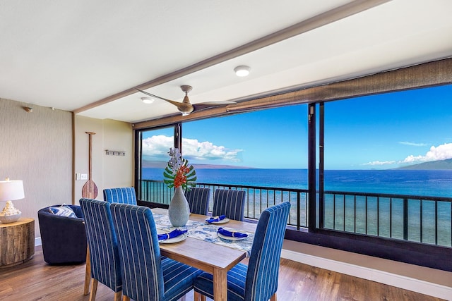 dining room with ceiling fan, a water view, and wood-type flooring