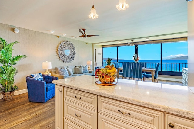 kitchen with light stone countertops, wood-type flooring, cream cabinets, a water view, and hanging light fixtures