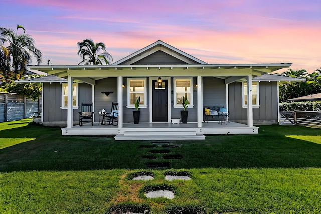 back house at dusk with a porch and a lawn