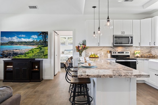 kitchen featuring white cabinetry, hanging light fixtures, stainless steel appliances, a kitchen bar, and decorative backsplash