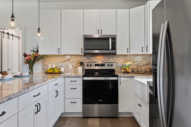 kitchen with light stone counters, stainless steel appliances, a barn door, and white cabinets