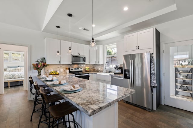 kitchen featuring appliances with stainless steel finishes, pendant lighting, sink, white cabinets, and a raised ceiling