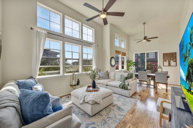 living room with a high ceiling, ceiling fan, and light hardwood / wood-style flooring