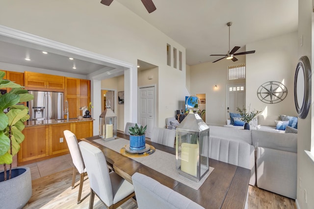 dining area with ceiling fan, sink, light hardwood / wood-style floors, and a towering ceiling